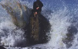 person on rock in waves is ignoring waves because he is numb to environemnt