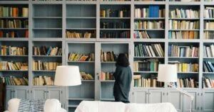 woman looking at all the stuff on her big bookshelf thinking about downsizing