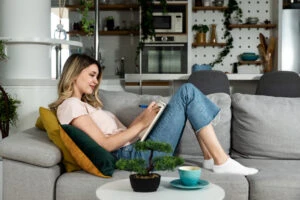 Young beautiful girl writing a love letter to her boyfriend or writing in the diary while she is smiling and sitting on the sofa in her room. Successful female having business ideas.