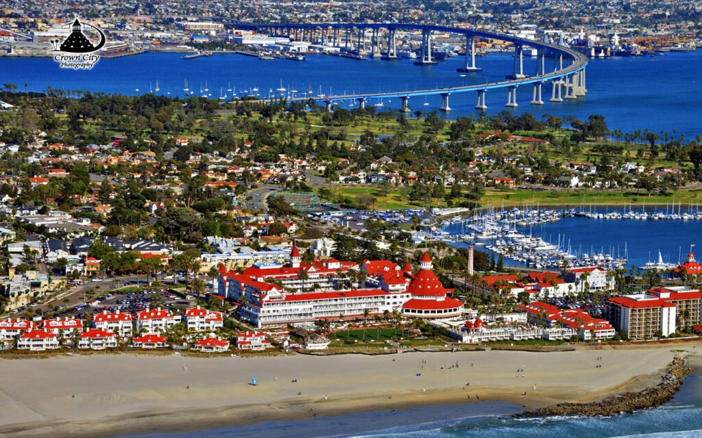 Aerial view of Coronado, CA, showcasing the iconic Hotel del Coronado, sandy beaches, and the Coronado Bridge.