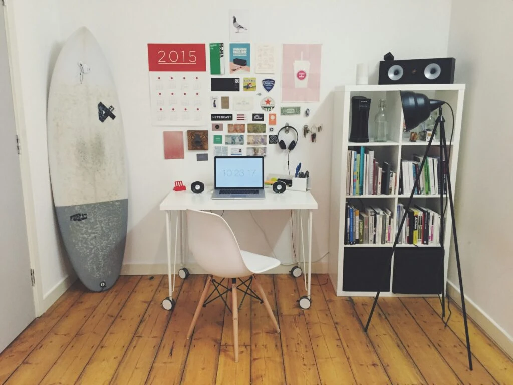 A clutter-free wooden desk in a sunlit room featuring an open laptop, notebook with pen, and steaming coffee cup, surrounded by a green plant and minimalist shelves—ideal for focused remote work.